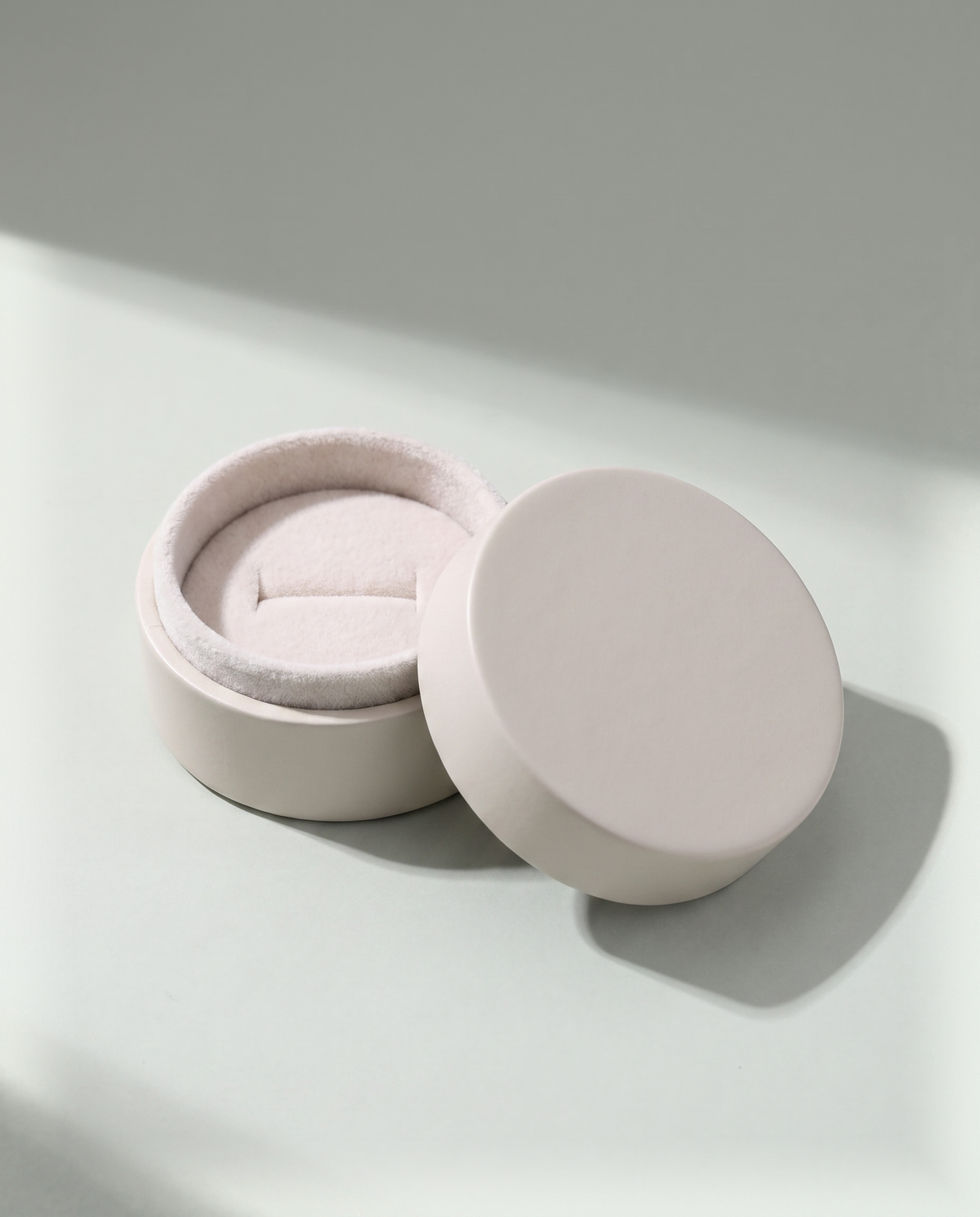 A small round ring box with its lid lifted off, empty, showing the soft lining inside