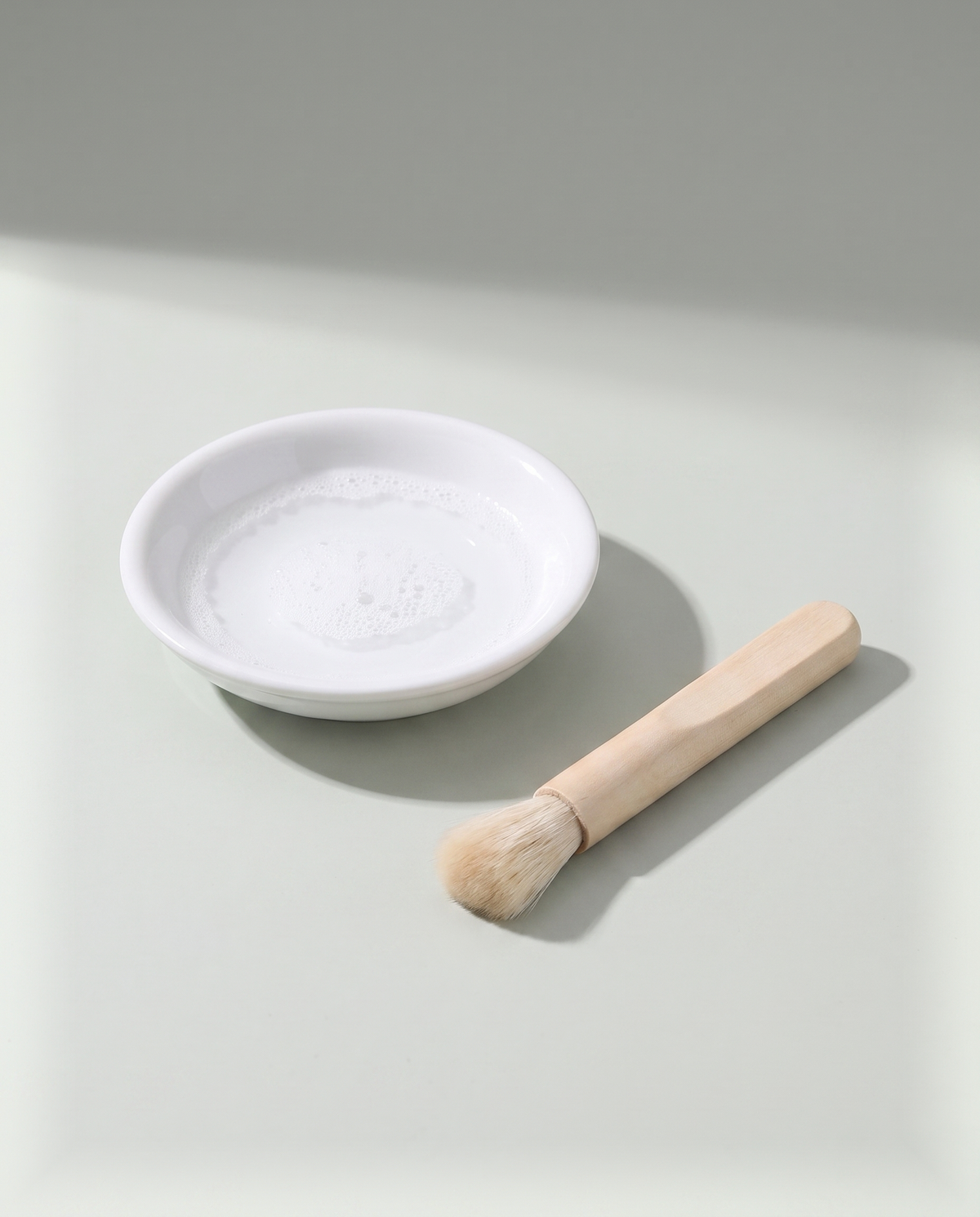 A shallow white dish of warm soapy water with a small soft-bristled brush lying beside it
