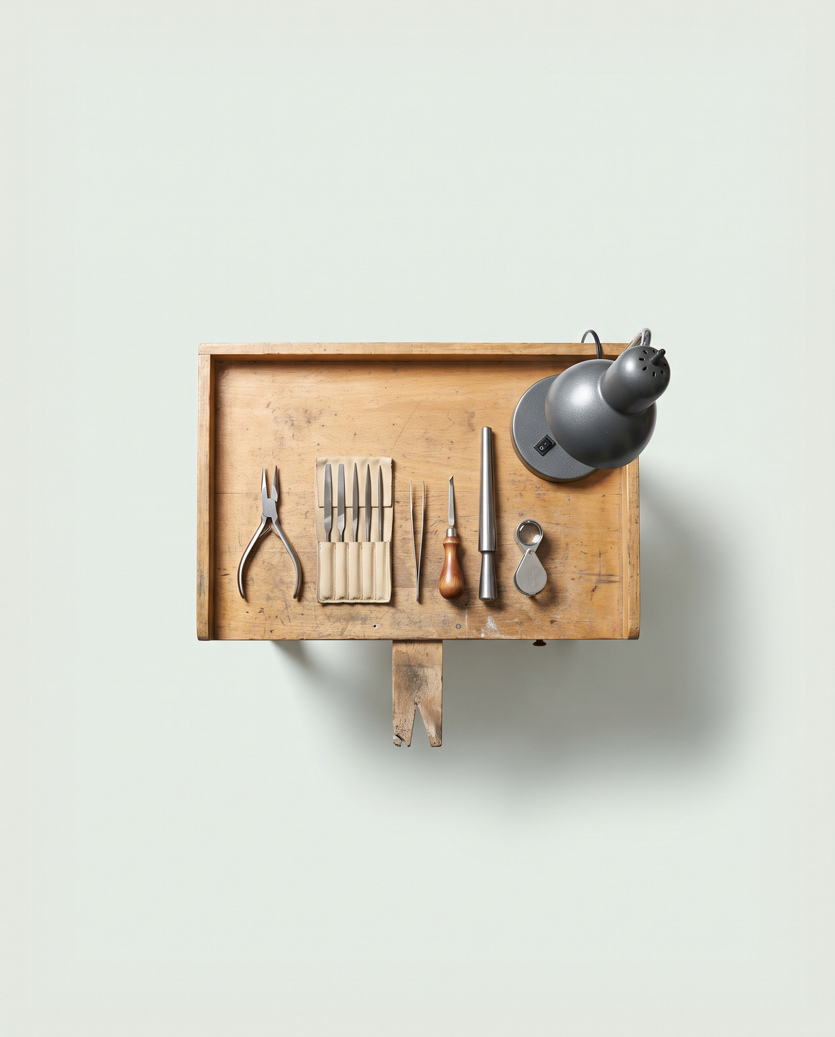 A jeweller's bench seen from above, hand tools laid out in a row beside the bench pin and a work lamp