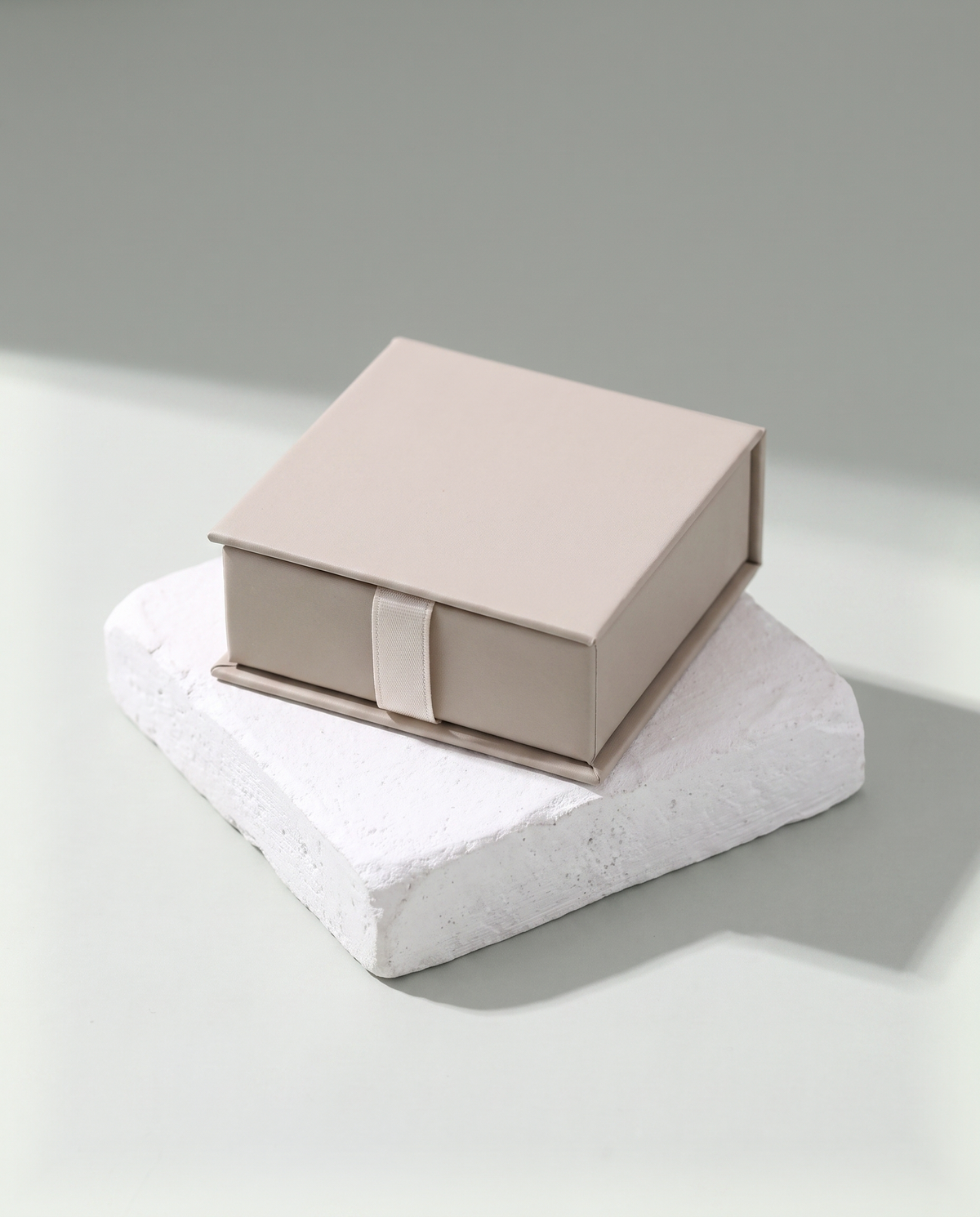 A small rigid jewellery box, closed and tied with a plain ribbon, resting on a white plaster block