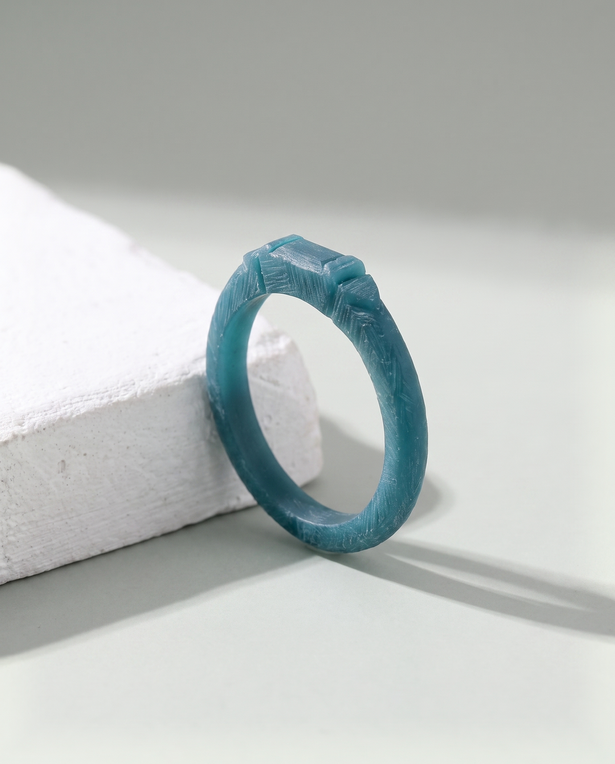 A ring pattern hand-carved in matte blue-green jeweller's wax, standing on a white plaster block