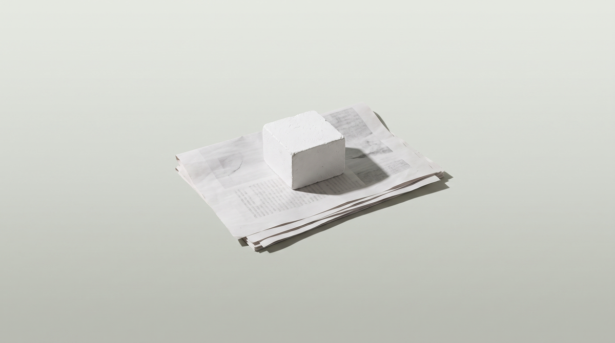 A stack of printed press clippings held flat under a plaster block