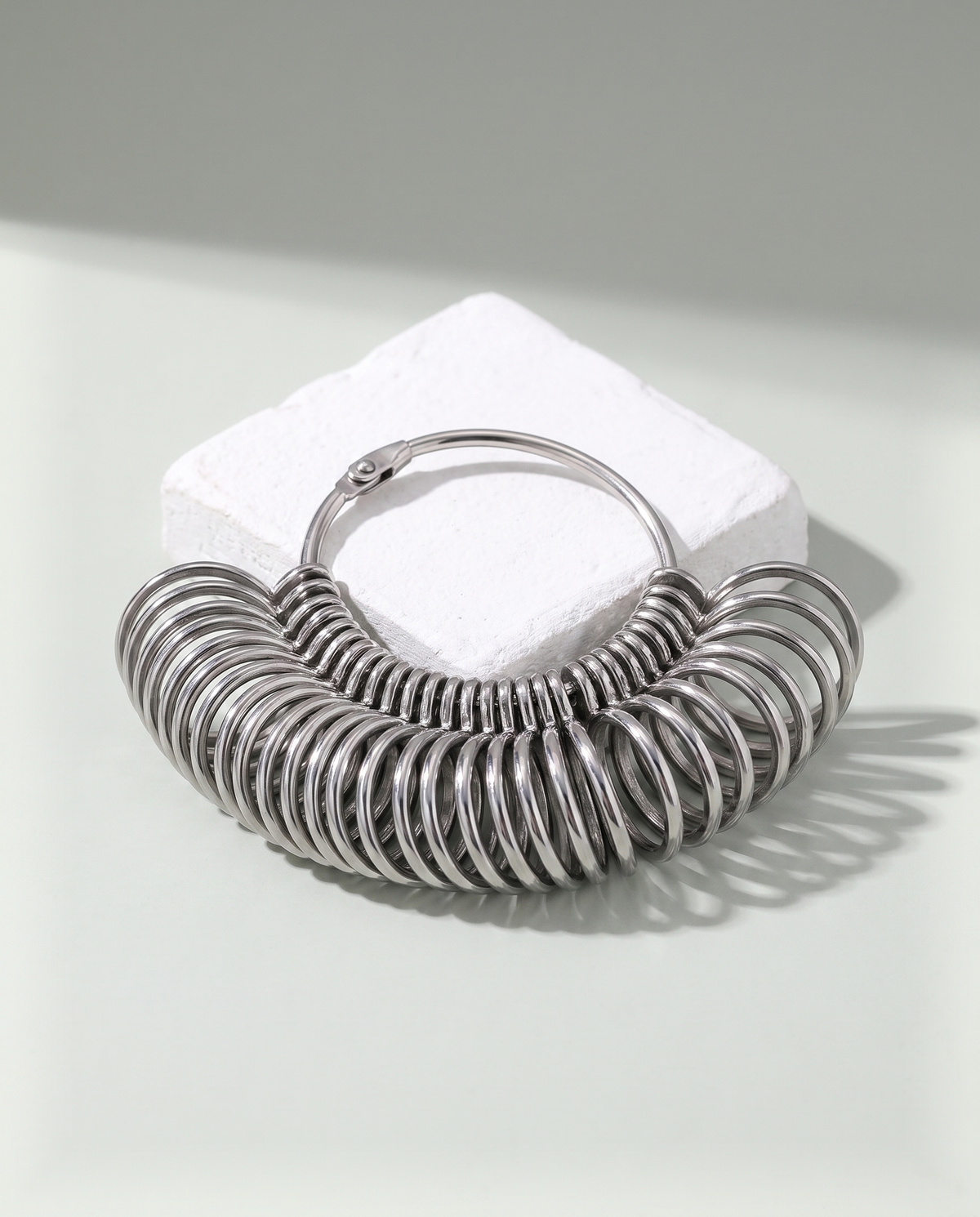 A set of blank steel ring sizing gauges fanned open on their hoop, resting on a white plaster block