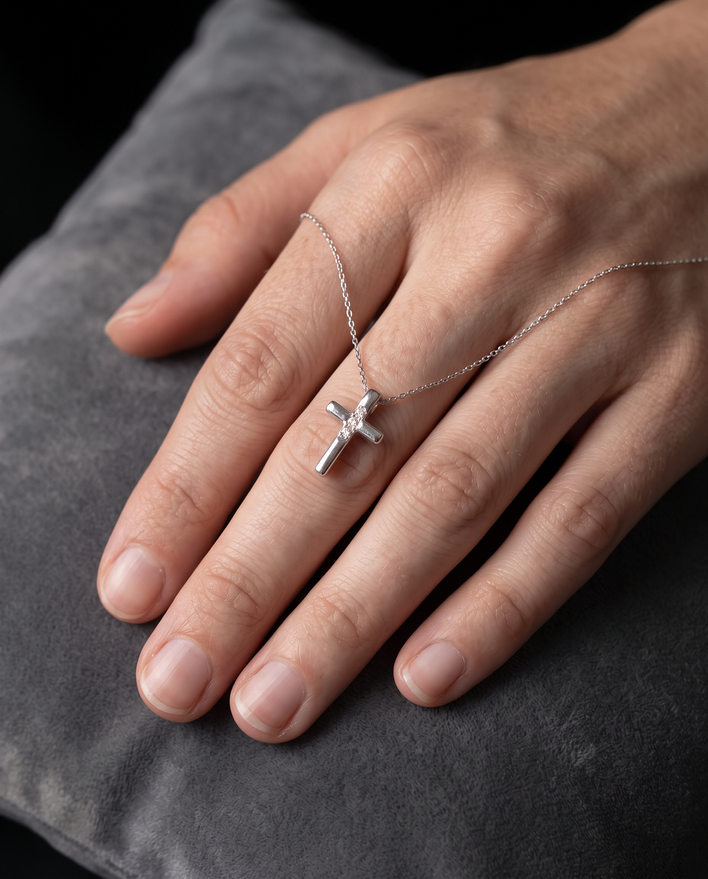 Small Cross pendant on its chain, worn draped across the back of a hand